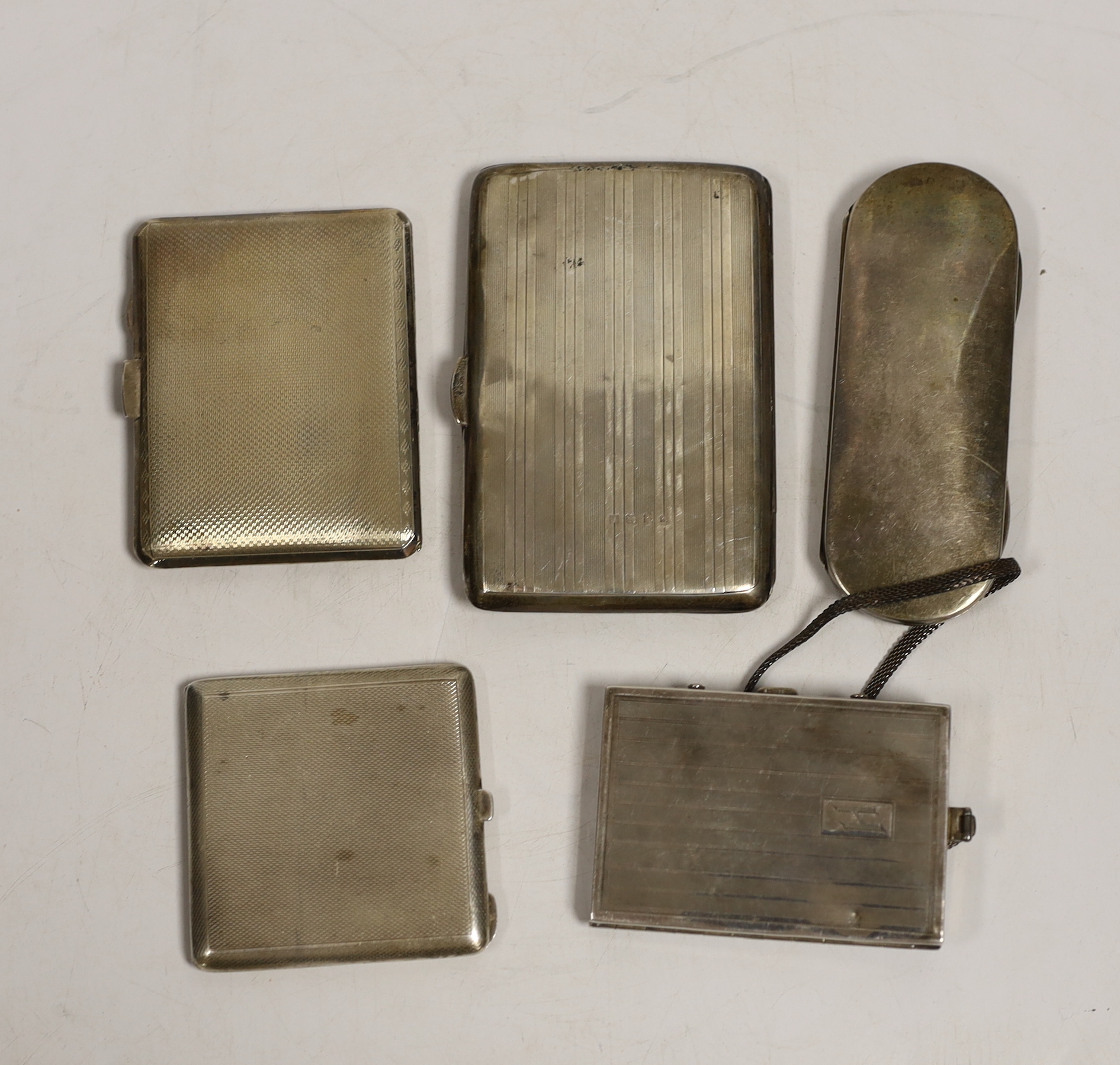 Two George V engine turned silver compacts, largest 83mm, a silver mounted aide memoire wallet, a silver spectacles case and a base metal compact.
